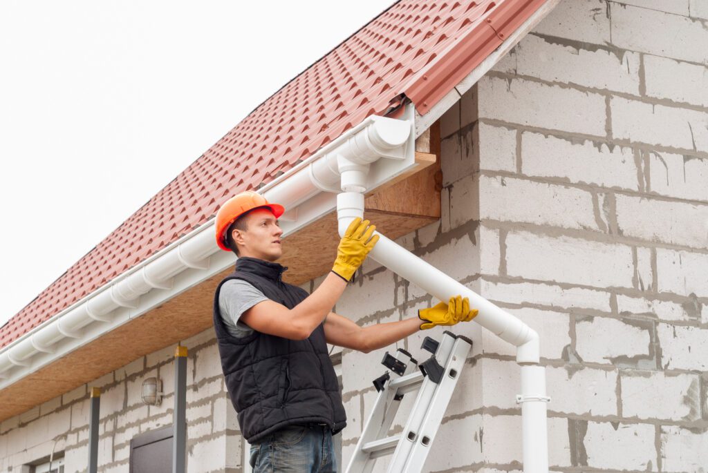 construction worker installs the gutter system on the roof to waterproof home
