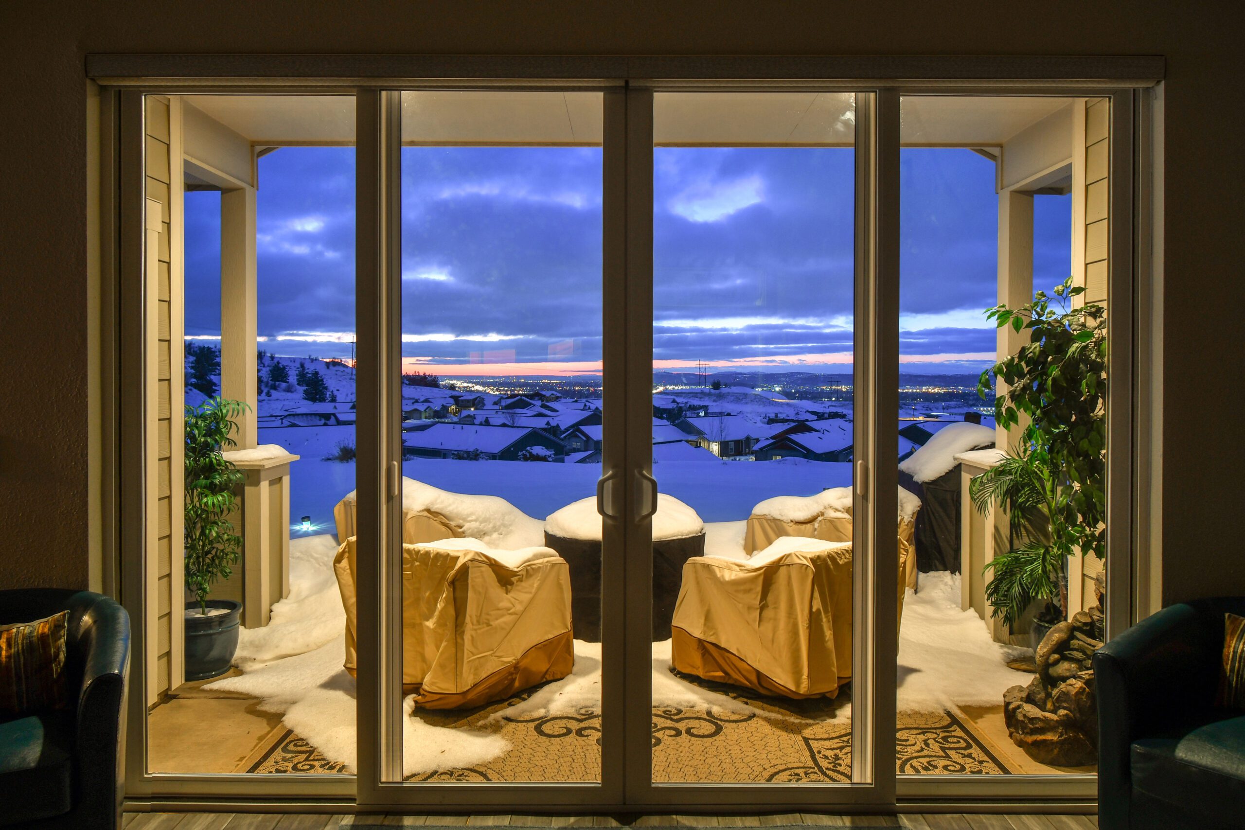 Hillside view from inside looking out to a outdoor patio covered in snow