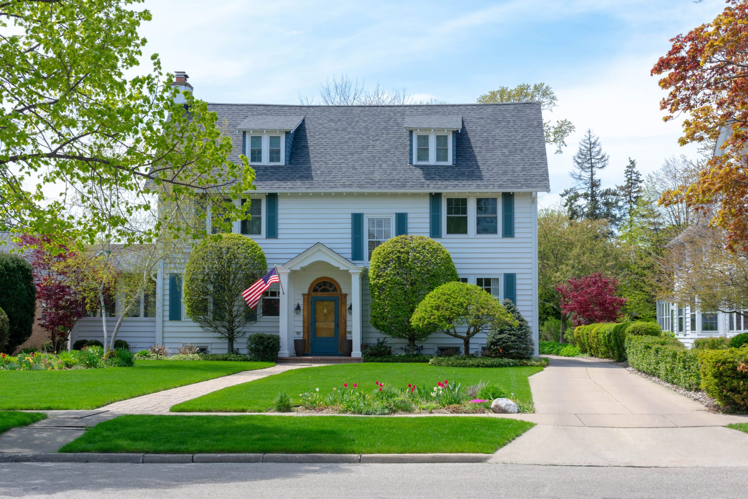 Front view of white house with blue shutters and American flag in suburban neighborhood